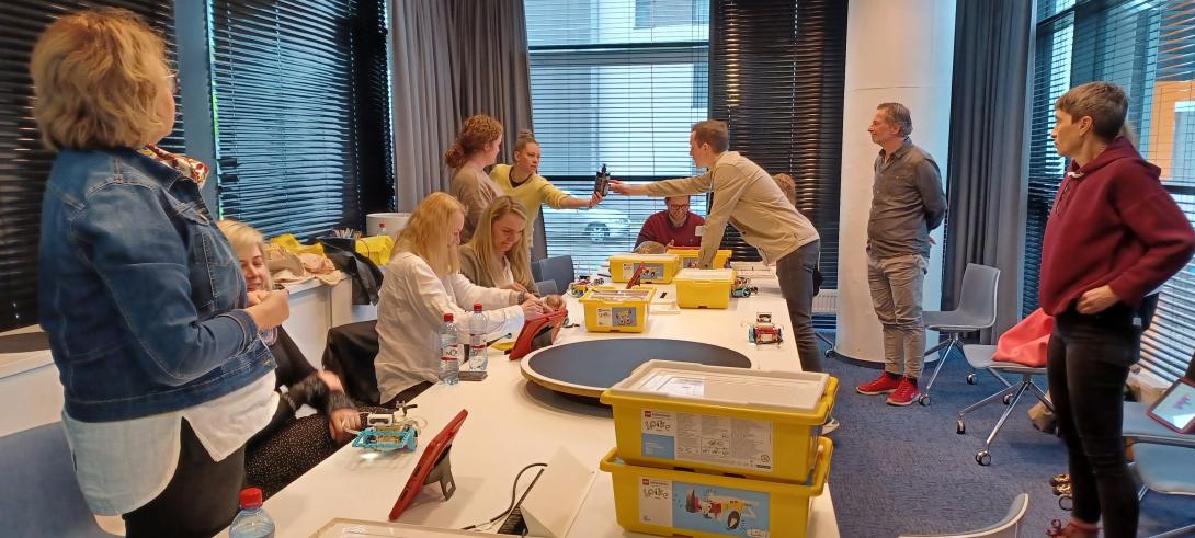 Group of People at a table, on it some boxes and iPads and Lego Roboter 